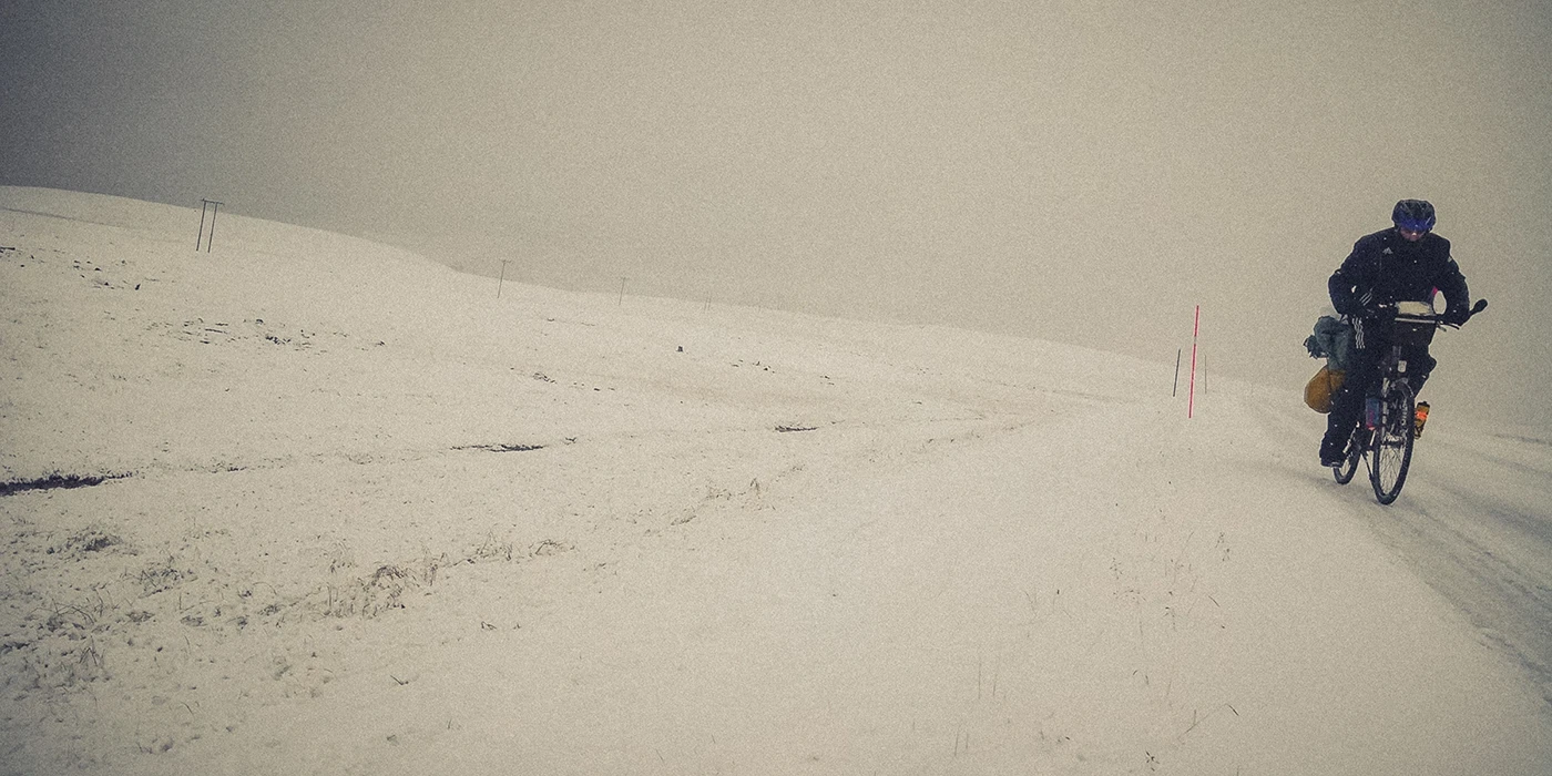 A bikepacker rides through extreme polar conditions on an icy road during a snowstorm