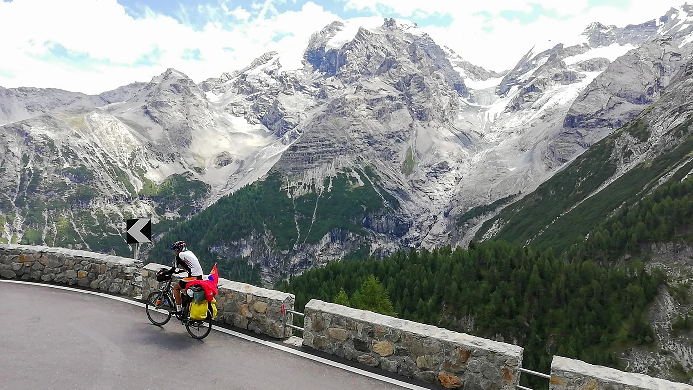 Cyclist riding uphill on the most challenging Alpine pass, Passo dello Stelvio, with snow-covered and icy Alpine peaks in the background
