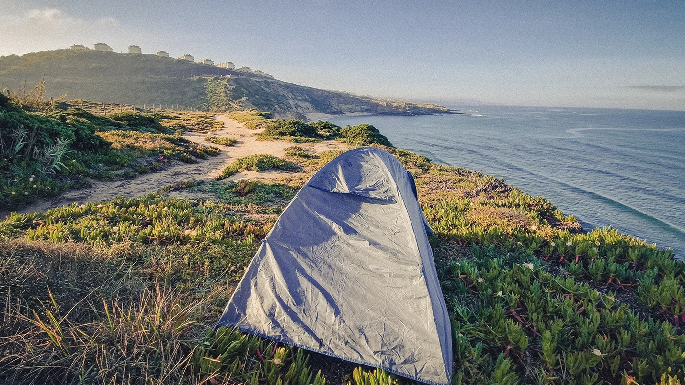 A tent perched on a cliff above Ribeira d’Ilhas Beach in Portugal, overlooking the Atlantic Ocean and the town of Ericeira.