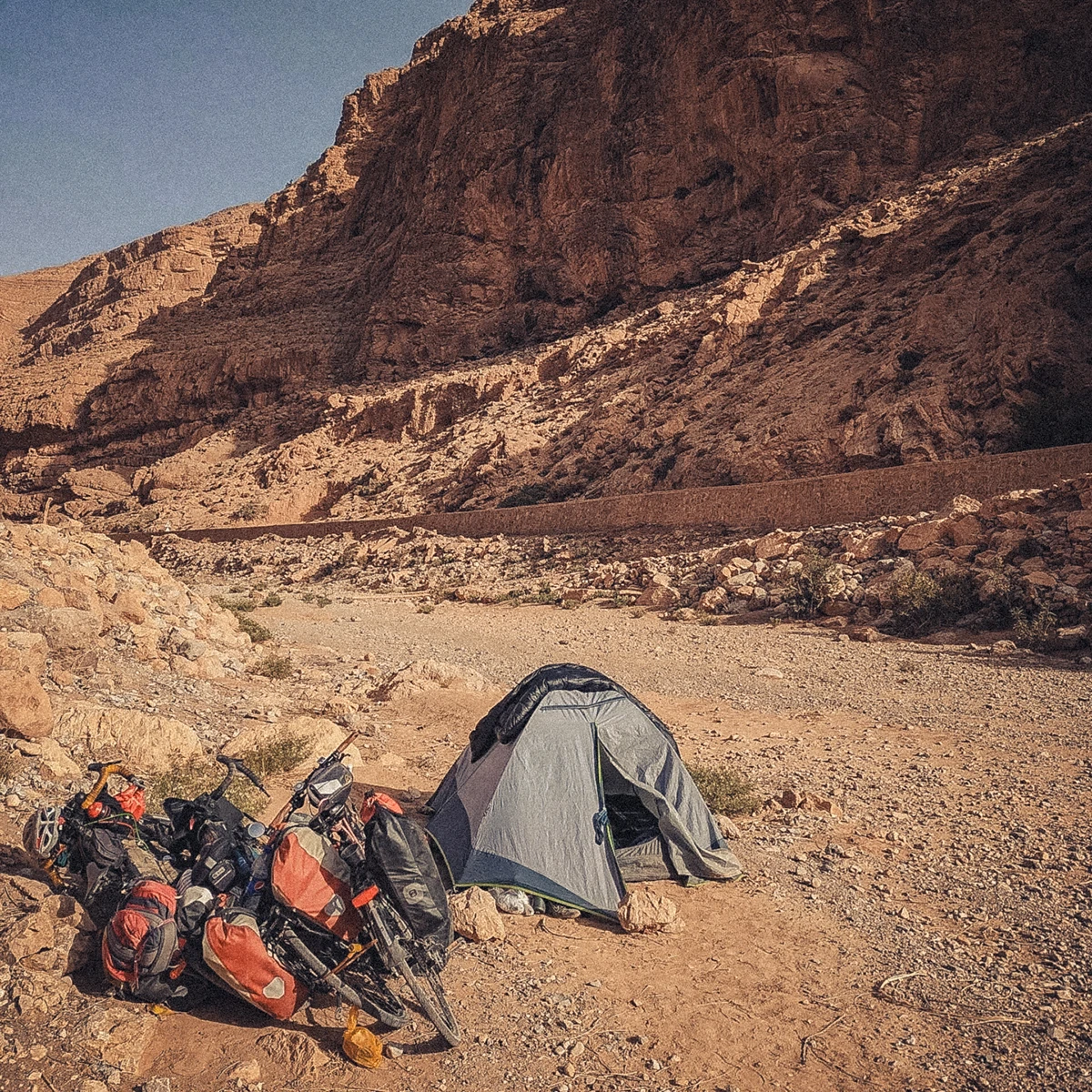 Camping in a tent within the dry, rocky Todra River canyon in Morocco, with bicycles left outside